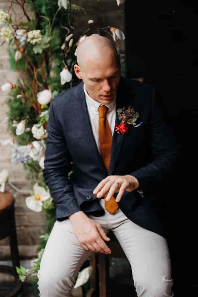 Well-dressed man in tailored suit at elegant wedding venue with floral backdrop.