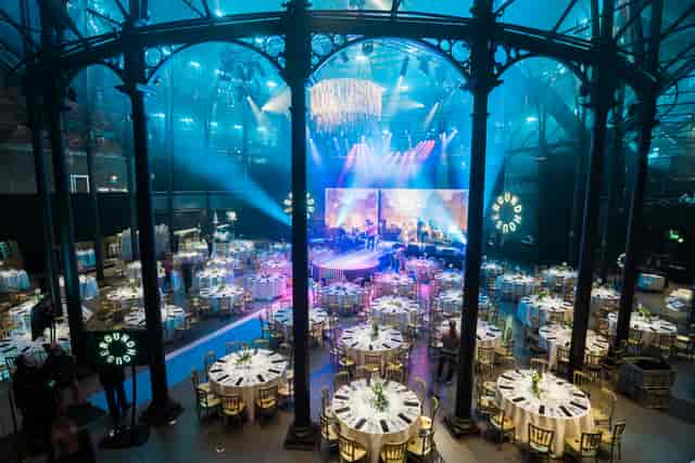 Elegant event space with round tables and floral centerpieces under a glass ceiling.