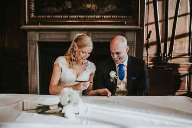 Couple joyfully signing marriage certificate in The Long Room, HAC wedding venue.