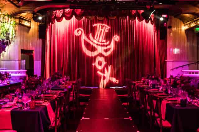 Vibrant gala event space with elegant stage and rich red curtains at The Box Soho.