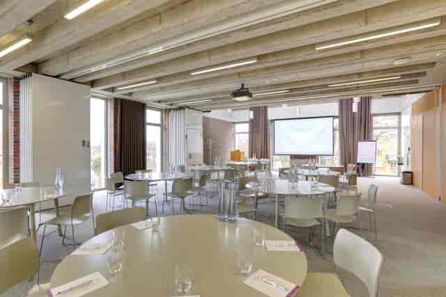 Buddy in a versatile meeting space with round tables, ideal for workshops and conferences.