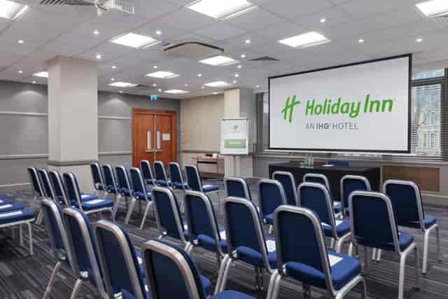 Warhol in modern Holiday Inn meeting room with blue chairs for presentations.