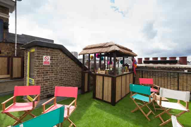 Vibrant rooftop event space with thatched bar and colorful seating for summer parties.