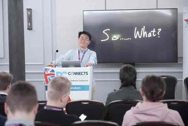 Speaker at conference in The Pasteur Room with engaging visuals and key message display.