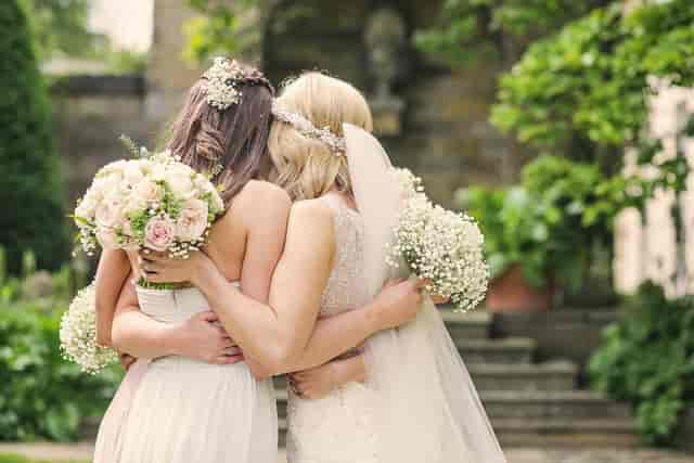 Brides embracing in a lush garden at Rudding Park wedding venue.