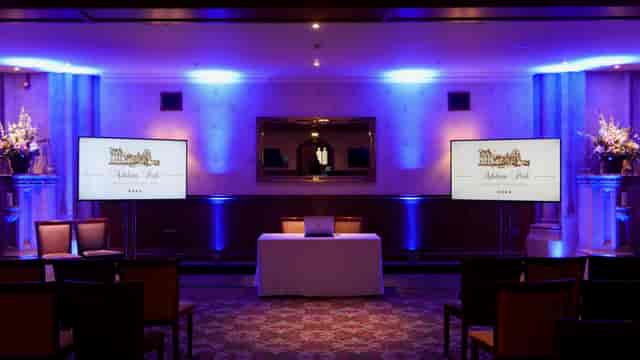 John Haywood presenting in a well-lit Ashdown Park event space with blue lighting.