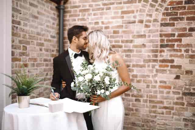 Couple celebrating wedding in The Colonnade, Pitzhanger Manor, with rustic brick backdrop.