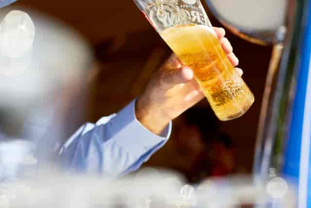 Hand holding a tall beer glass at Lifehouse Spa gardens for event planning.