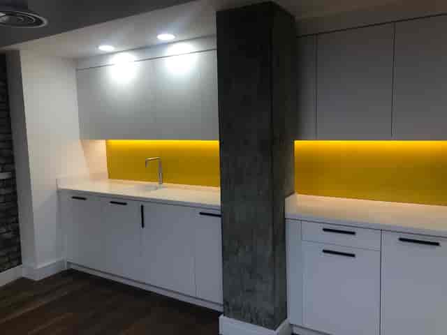 Modern kitchenette with white cabinetry and yellow backlighting for events and meetings.