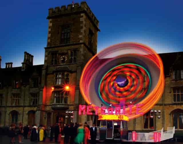 Vibrant outdoor event at Royal Agricultural University with spinning attraction and dynamic lighting.