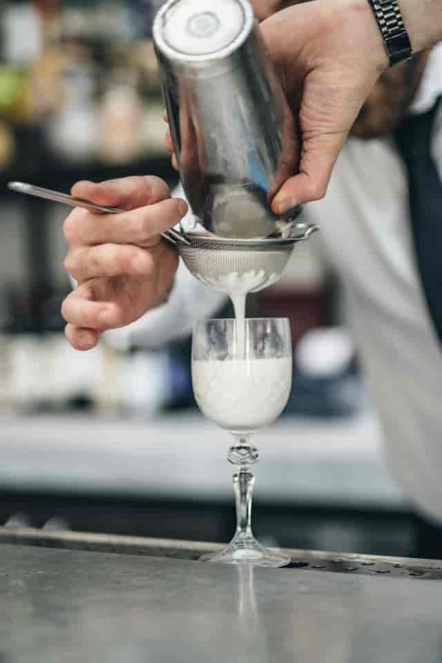 Bartender straining cocktail at TOZI Restaurant & Bar for elegant event catering.