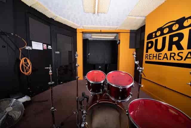Rehearsal space with drum set, vibrant orange wall for music events and performances.