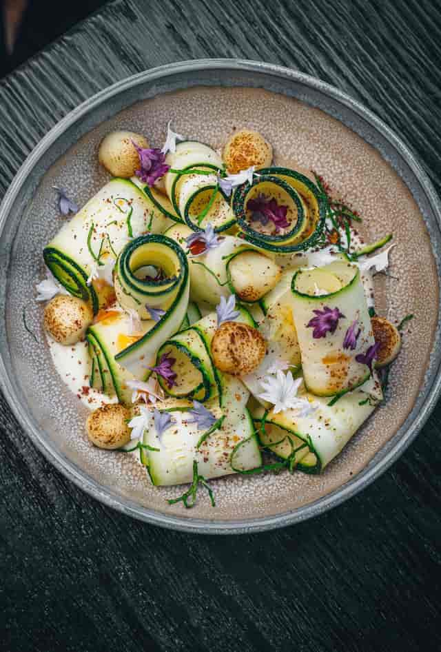 Elegant zucchini ribbons dish with edible flowers at Arros QD event catering.