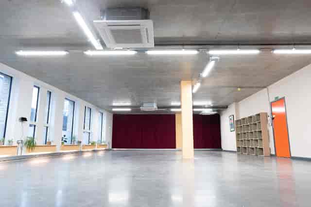 Versatile event space with natural light and red curtain, perfect for workshops and seminars.