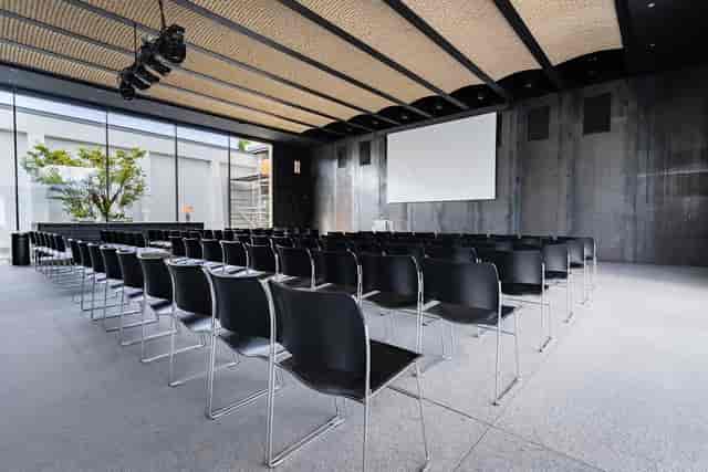 Modern event space in Mogens Dahl Koncertsal with black chairs and projection screen.