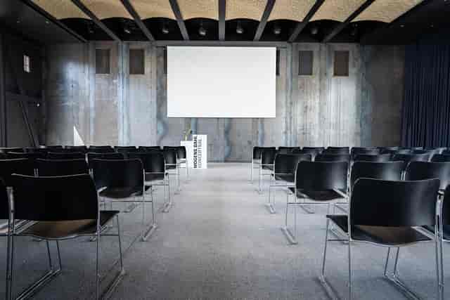 Modern event space with black chairs and large screen, ideal for conferences and workshops.