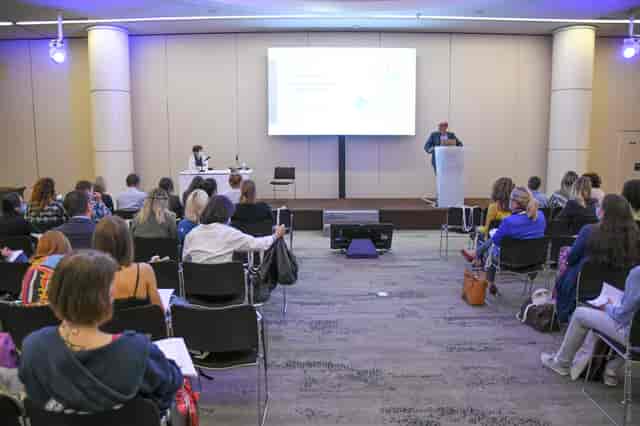 Professional conference with speaker engaging audience in well-lit room, ideal for networking.