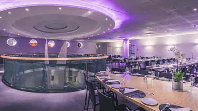 Modern event space with round tables and purple lighting for corporate meetings and gatherings.