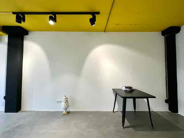 Minimalist urban hotel event space with sleek black table and bright yellow ceiling.