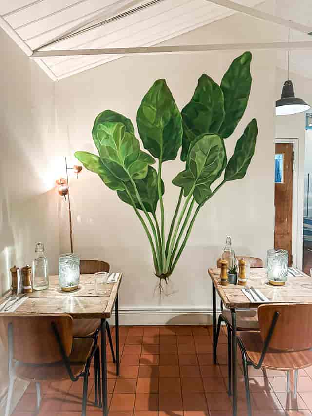 Stylish dining venue in Spinach East Dulwich with vibrant leaf mural, perfect for events.