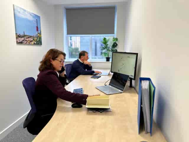 Focused professionals in a hybrid meeting with dual screens and plants for warmth.