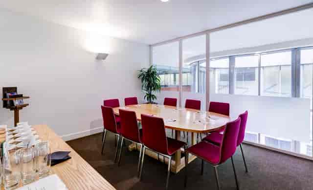 Modern meeting room with wooden table and red chairs, ideal for collaborative events.