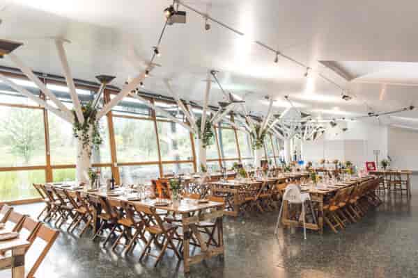 Contemporary glass-walled event space with wooden tables, ideal for weddings and corporate events.