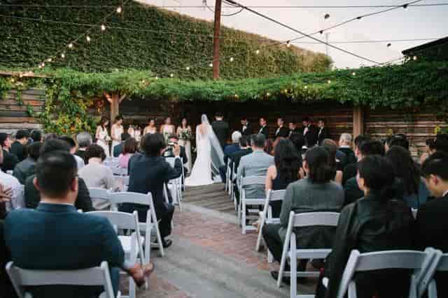 Outdoor wedding ceremony with couple at altar, string lights, and lush greenery.