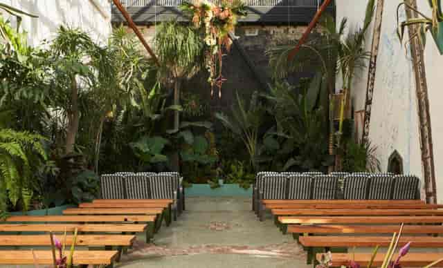 Greenhouse Courtyard in DTLA: serene outdoor event space with wooden benches and lush greenery.
