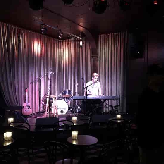Cozy Hotel Cafe Main Stage set for intimate live music event with piano and candles.