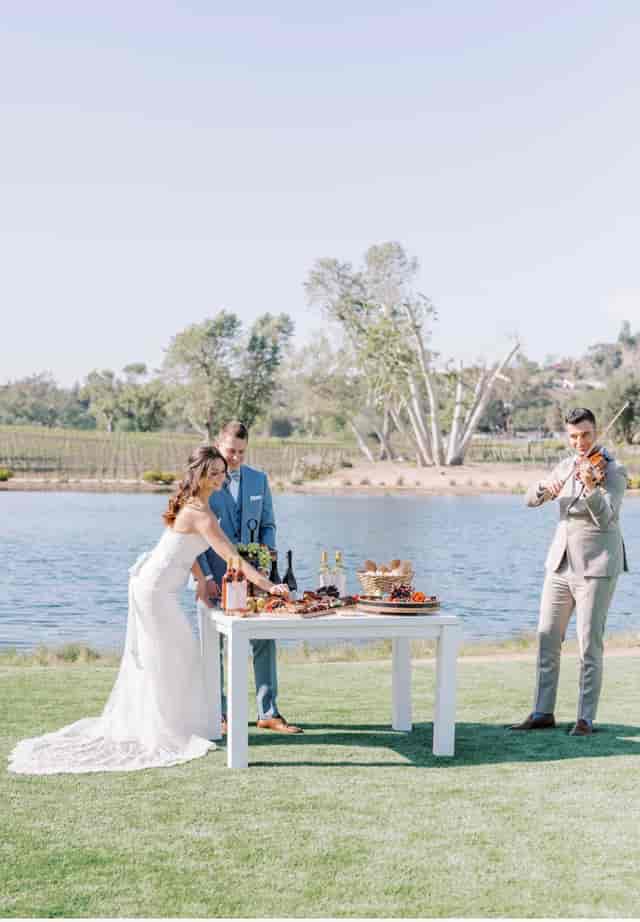Elegant outdoor wedding setup by a lake with gourmet food and live music.