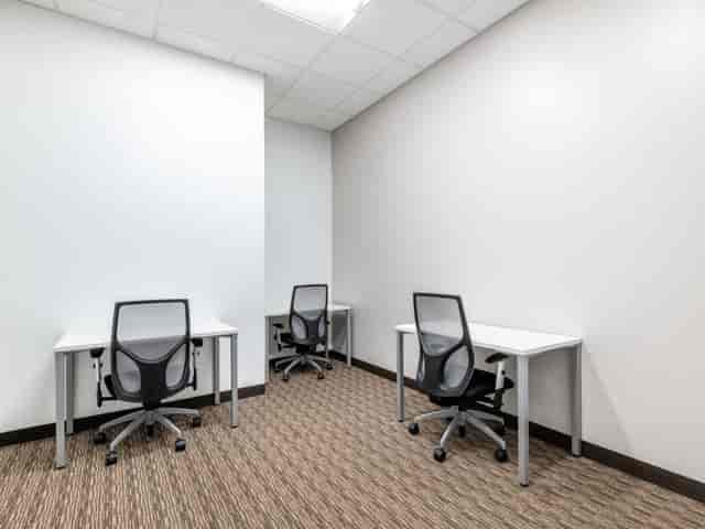 Minimalist coworking meeting space with three workstations for focused discussions.