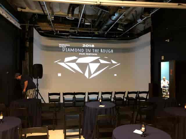 Event space with black chairs and projection screen for Diamond in the Rough Film Festival.