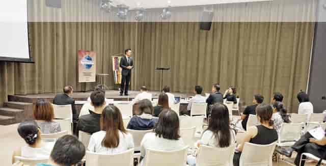 Speaker engaging audience in well-lit LISHA Tamil Toastmasters Club conference room.