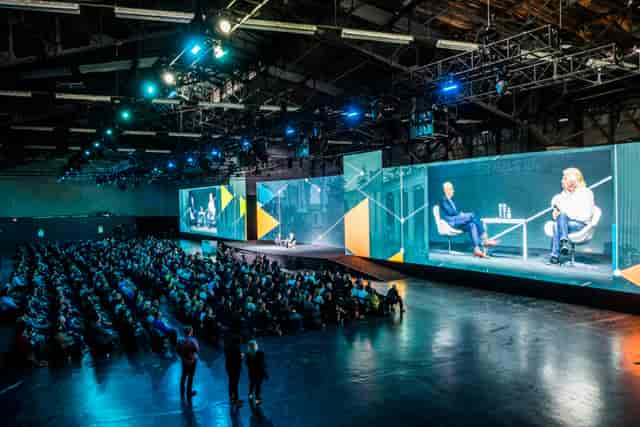 Large event at Storek NPU Venue with engaged audience and dual screens for presentations.