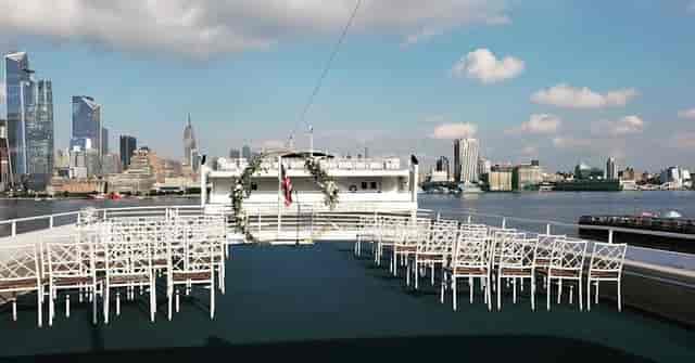 Outdoor gala on a boat with white chairs and skyline backdrop for weddings and fundraisers.