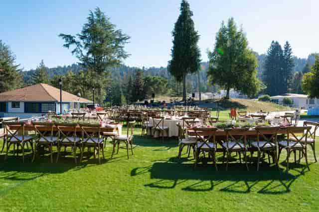 Outdoor event space with long wooden tables on lush grass for garden parties or retreats.