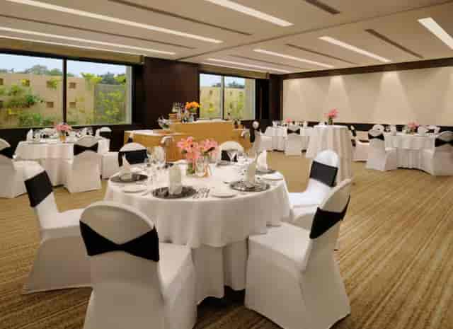 Elegant event space at Hilton Embassy Golf Link Bengaluru with round tables and floral centerpieces.