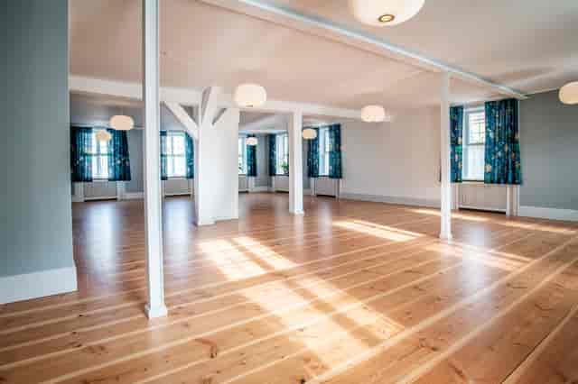 K. Larsen in a spacious, well-lit event space with wooden flooring for gatherings.