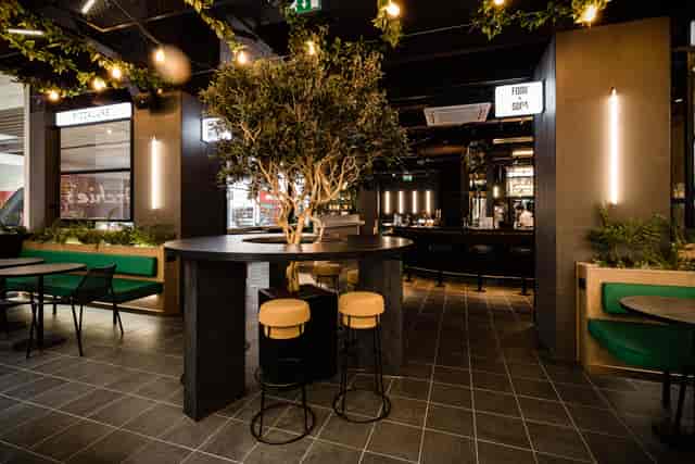 Modern event venue with central bar and greenery, ideal for corporate meetings and social functions.