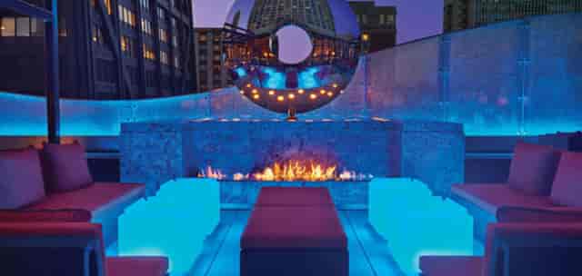 Rooftop bar at The Ritz-Carlton, Chicago with modern seating and vibrant blue lighting.