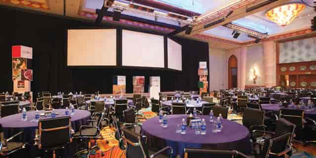 Ballroom at Almas Conference Centre set for corporate meetings with round tables and screens.
