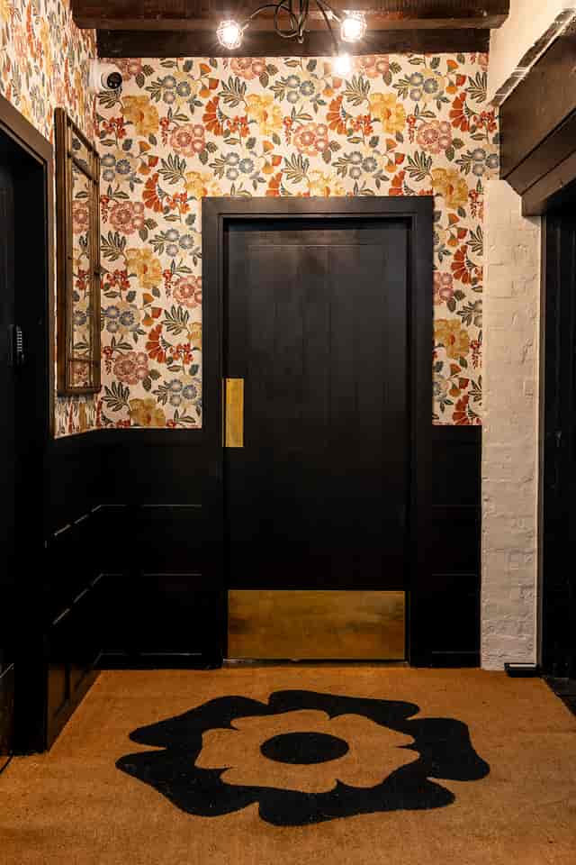 Tudor Barn Eltham entrance with dark wooden door and floral wallpaper, perfect for events.
