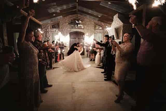Bride and groom send-off with sparklers in rustic ballroom venue decor.