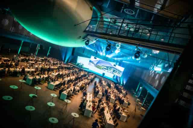 Event setup in Umwelt Arena Schweiz with banquet tables and stage under green lighting.
