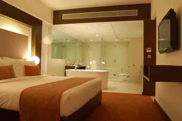 Modern hotel suite at Pride Hotel Bangalore, featuring a comfy bed and glass-walled bathroom.