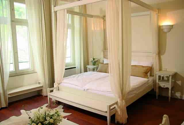 Four-poster bed in serene Hotel Villa Marstall room for retreats and gatherings.