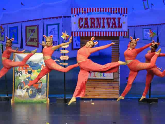 Colorful gymnasts perform in a festive carnival-themed dance show at a studio event.