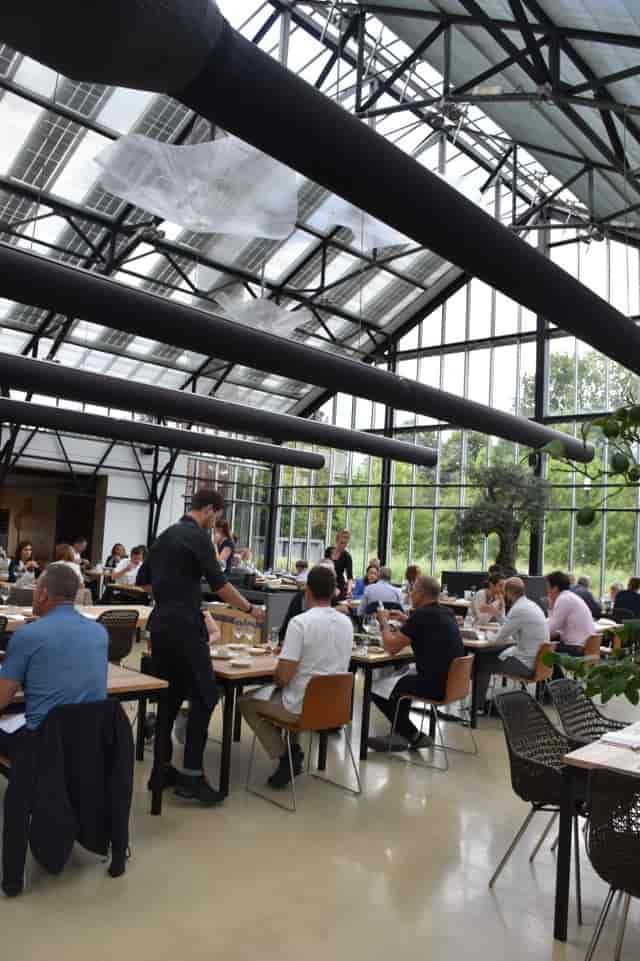 Modern glass-walled event space with tables for corporate gatherings at Restaurant De Kas.