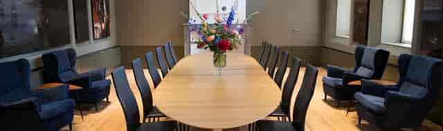 Admiralty boardroom at Het Scheepvaartmuseum, featuring a sleek wooden table and floral decor.